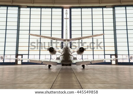 Private corporate jet parked in a hangar facing away from the camera towards the doors in an aviation, travel and transport concept