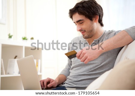 View of a Young relaxed man paying online with credit card in sofa