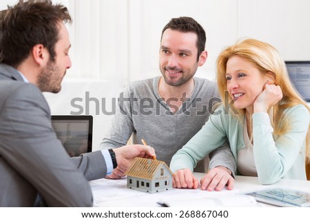 View of a Real estate agent present project on miniature house to a young couple