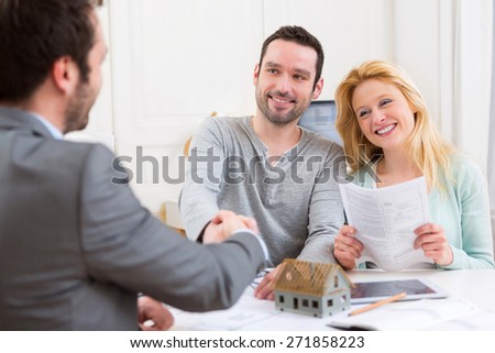View of a Young happy couple handshaking real estate agent after signing contract