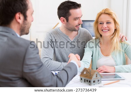 View of a Young happy couple handshaking real estate agent after signing contract