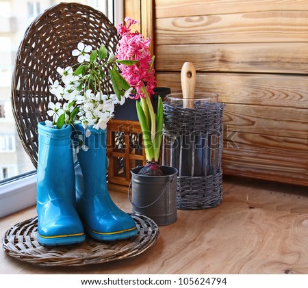 Sprig of flowering cherry in a dark blue rubber knee-boot and pink hyacinth on the window of balcony. Infatuation for gardening on a balcony