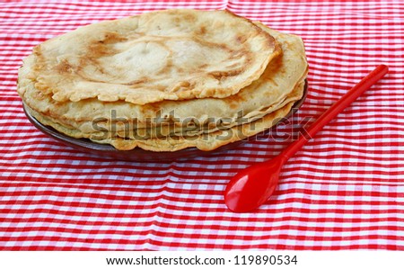 Pile of pancakes on a red dish and with a red spoon. Shrovetide