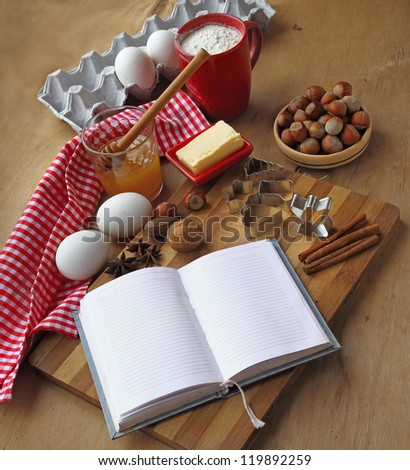 Open culinary book with a towel, butter, cup of flour, egg and pie-pans