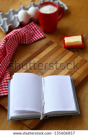 Opened notebook for the recipes and  butter, eggs,  flour on a cook-table