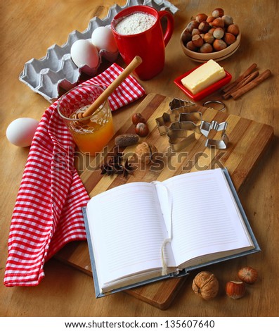 Opened book for the records of recipes and honey, butter, eggs, nuts, cinnamon, flour on a cook-table