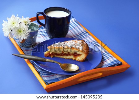 Breton butter cake with quince jam stuffing, sprinkled with coconut crumb on blue plate and a bouquet of white chrysanthemums on a blue background
