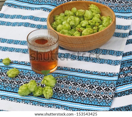 A glass with a drink of hops on the background of traditional Ukrainian embroidered towel and  branch of hops
