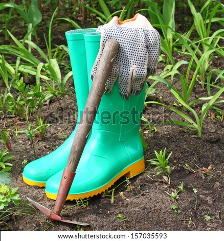 Green rubber boots for working in the garden and rake against the flowerbeds