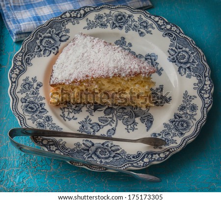 Portion biscuit with coconut on the vintage English plate, next to the food tongs