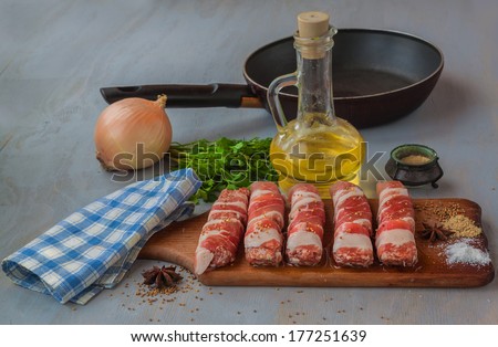 Raw meat loafs and piece of meat on a plate next to the spices and oil a frying pan on the kitchen table.