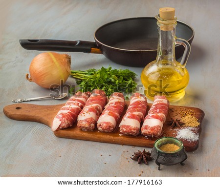 Cooking of lunch on meat rolls on a cutting board on a background of the frying pan, sunflower oil and onions with spices