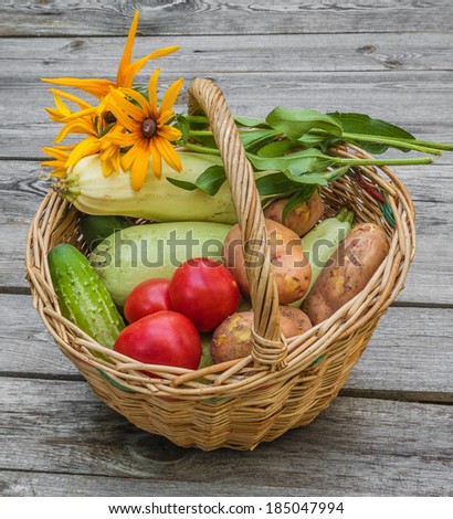 Basket with tomatoes, cucumbers, zucchini, potatoes and a bouquet of yellow rudbeckia on a wooden table