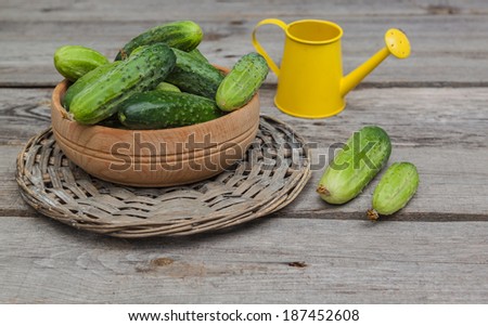 Cucumbers in a wooden bowl on a background of yellow watering can on an old wooden table