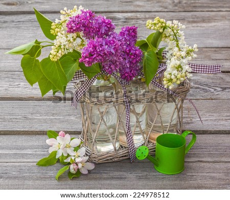 Bouquet of blooming lilacs and apple trees near decorative watering can on a wooden table