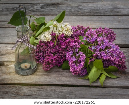 Bouquet of lilacs and light with a burning candle in the evening on a wooden table