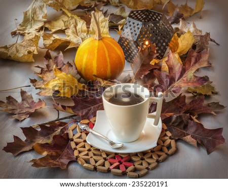 Cup of coffee on a wooden table with fallen leaves, burning candle and pumpkins