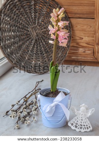 Spring still life with pink hyacinths in a decorative bucket with bow and angel on the window and willow twigs