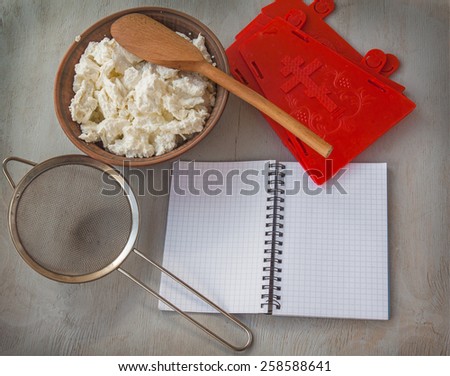 Notebook to write the recipe a bowl of cottage cheese, sieve and shape for Easter cheese on the kitchen table