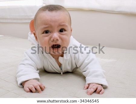 Beautiful baby boy crying on bed.