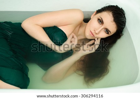 Beautiful young sexy girl with dark hair wet, evening makeup, takes bath with perfect skin in romantic atmosphere, beauty cosmetic salon and spa for woman