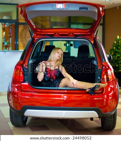 nice white girl sitting in luggage carrier of new red car in office