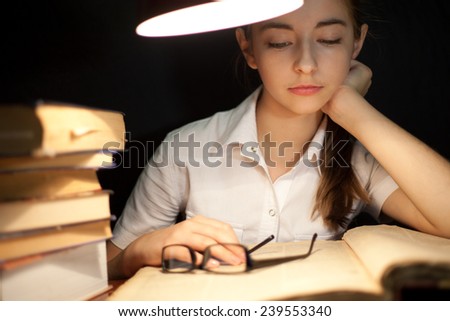 Young girl reading book under lamp in the dark