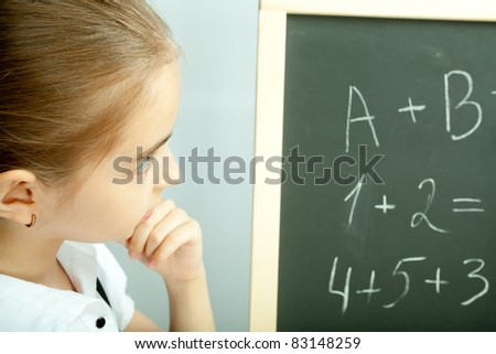 School girl looking at the blackboard with exercises and thinking about answers