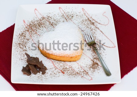 A heart shaped cake presented on a white plate with chocolate garnish