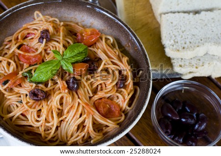 A plate of spaghetti with italian sauce, served with red wine, bread and olives on a wooden table