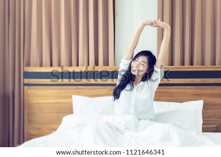 Beautiful Asian woman waking up on her bed in the bedroom, she is stretching and smiling after wake up, Asia women exercising in the morning, feels refreshed.good dream last night, lifestyle in home