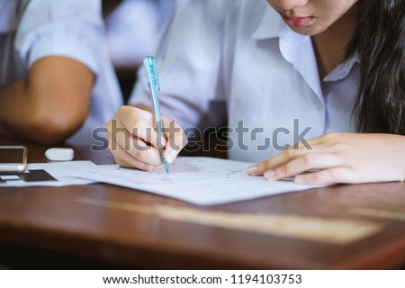 Student hand holding pen writing doing examination in university ,girl in uniform attending exam classroom educational school: college people in room ,Scholarship test for Study abroad