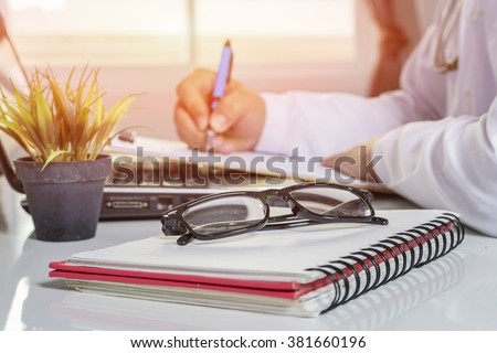 glasses on note book ,Doctor at work,  male doctor write prescription,medical record and computer on the table.,Doctor office table desk,and other things on wooden desk background.selective focus