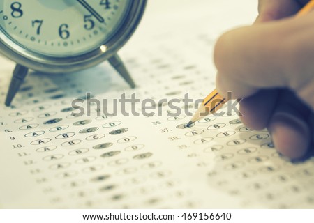 A pencil sitting on a test bubble sheet and alarm clock, optical form of an examination,Answer sheet with pencil,Standardized test form with answers bubbled and a black pencil,selective focus,vintage