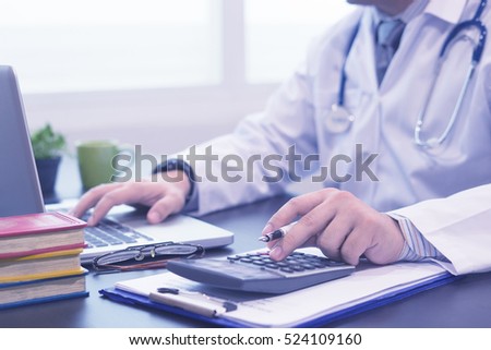 young medical doctor caucasian healthcare professional wearing a white coat with stethoscope in hospital ,calculates on an electronic calculator for doctor fee,selective focus,blue color tone