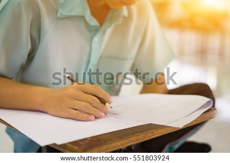 Student hand holding pen writing doing examination with blurred abstract background university  boy  in uniform attending exam classroom educational school:  college people in room vintage color