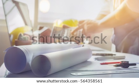 filled with building plans and background of Town planning,architect man working with laptop and blueprints, architects sitting from behind working on architectural plan by calculator