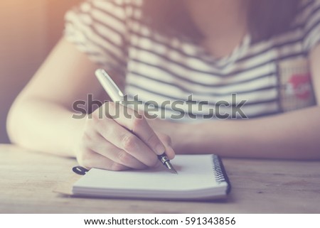 Student hand holding pen writing doing examination in university ,students in uniform attending exam classroom educational school: Young female student writes information from portable net-book