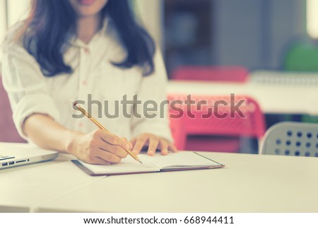 Student hand holding pencil writing doing examination in university ,students in uniform attending exam classroom educational school: Young female business writes information from portable net-book