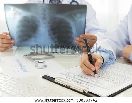Doctors records data and looking film X-Ray in office of hospital.