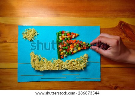 Applique of food in the form of a ship at sea on a blue cloth on a wooden kitchen table (soft focus)