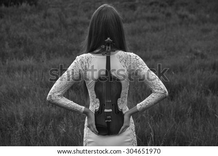 Beautiful female (girl, model) with big eyes and dark hair in a white dress playing the violin in the field and summer forest