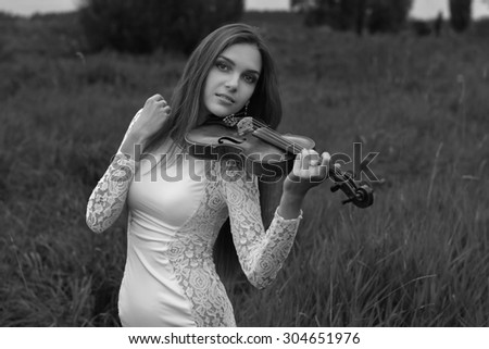 Beautiful female (girl, model) with big eyes and dark hair in a white dress playing the violin in the field and summer forest