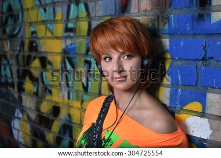 Beautiful redhead girl with freckles  near graffiti wall listening to the sound of music in the headphones