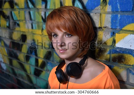 Beautiful redhead girl with freckles near graffiti wall listening to the sound of music in the headphones