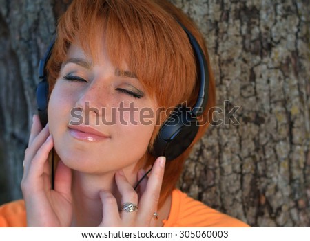 Beautiful redhead girl with freckles in a park listening to the sound of music in the headphones