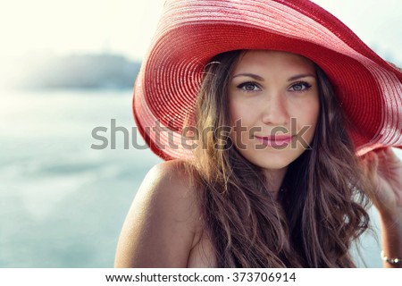 Beautiful girl in a red hat smiling at the summer waterfront