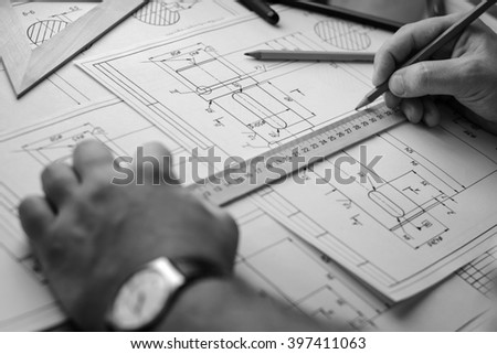 Man architect draws a plan, graph, design, geometric shapes by pencil on large sheet of paper at office desk. Soft focus. Black and white