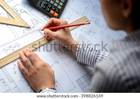 Girl architect draws a plan, graph, design, geometric shapes by pencil on large sheet of paper at office desk. Soft focus. Vignette
