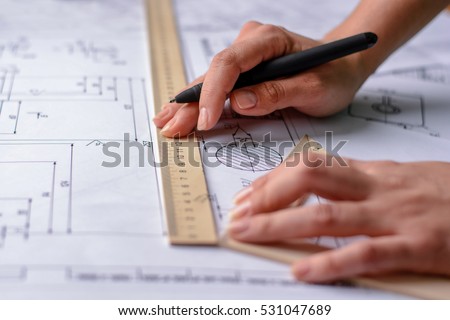 Girl architect draws a plan, graph, design, geometric shapes by pencil on large sheet of paper at office desk.